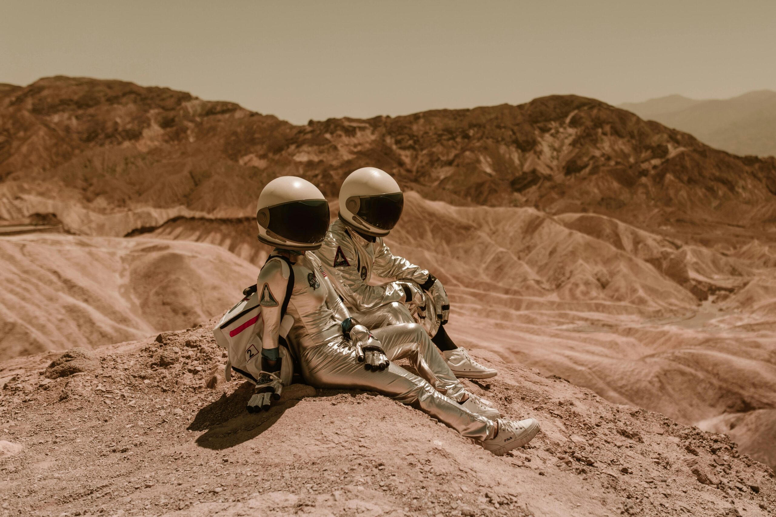 Two astronauts in silver suits sitting on a barren desert landscape, exploring new realms.